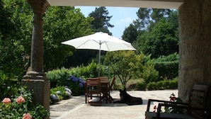 A covered patio area with a stone floor, a wooden bench, a table, and an umbrella providing shade. - Cete: house / villa - Cête (Cête)