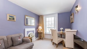 A room with a grey sofa, a dining table with chairs, a fireplace, and a window with curtains. - Fern House, Grassington; central yet parking & quiet, light & period elegance (Grassington North Yorkshire)