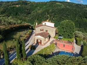 A stone villa with a swimming pool, surrounded by lush greenery and hills.