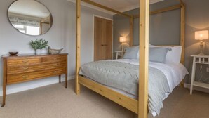 A four-poster bed with a wooden frame, a bedside table with a lamp, a wooden dresser with drawers, and a round mirror on the wall. - Kipling House (6), Wells-next-the-Sea, Norfolk (Wells-next-the-Sea)