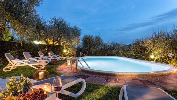 A swimming pool with lounge chairs and candles, surrounded by greenery.