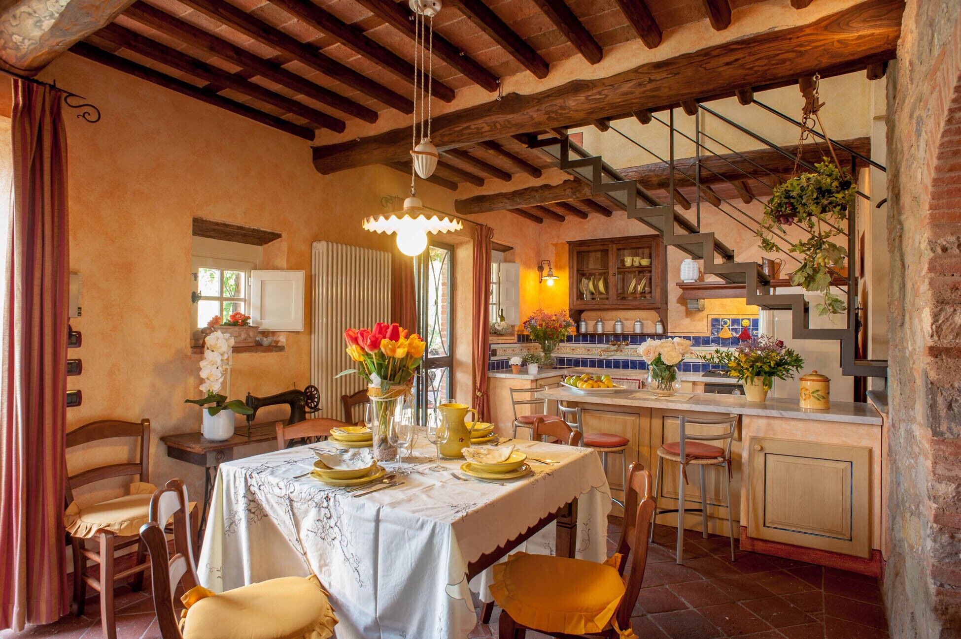 A rustic kitchen with wooden beams, a dining area with a table set for four, and a staircase leading to an upper level.