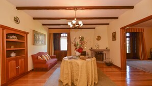 A room with a wooden floor, a red sofa, a table with a tablecloth, a fireplace, and a chandelier.