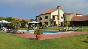 A large house with a swimming pool, outdoor furniture, and a well-maintained lawn.