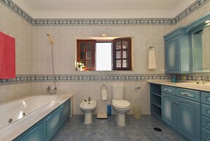 Un baño con bañera, bidé, inodoro y armarios azules.