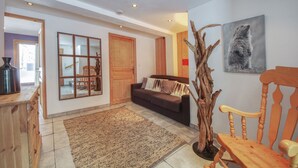 A spacious living area with a large window, a wooden rocking chair, a brown sofa, and a wooden cabinet.