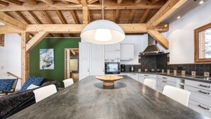 A modern kitchen with a large island, white cabinets, and a wooden ceiling.