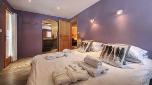 A bedroom with a large bed, two pillows with feather designs, a wooden door, and a small table with a lamp.