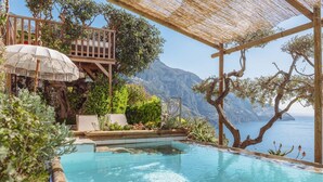 A pool area with a wooden deck, lounge chairs, and a view of the sea.