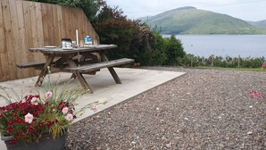 A picnic table with a coffee maker and a milk carton, surrounded by a gravel area and flower beds.