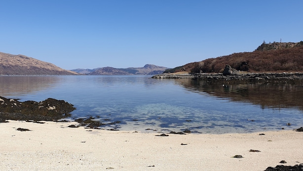 A calm lake with a sandy beach and rocky shoreline.