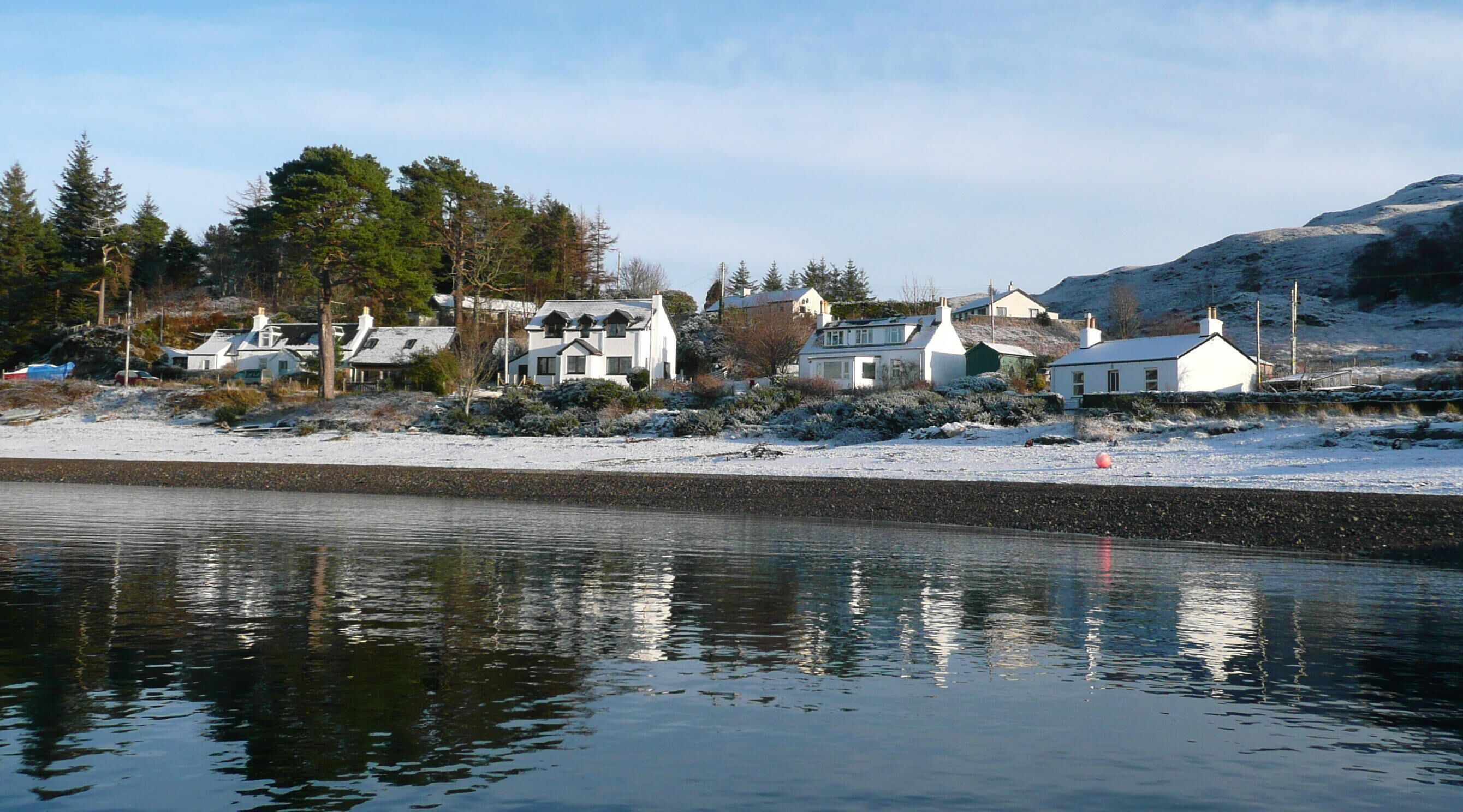Une propriété située au bord de l’eau, comprenant plusieurs maisons, un paysage enneigé et une étendue d’eau calme dans laquelle se reflètent les bâtiments.