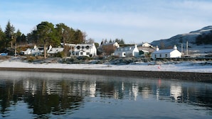 A waterfront property with multiple houses, a snow-covered landscape, and a calm body of water reflecting the buildings.