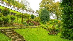 A lush garden with stone steps leading up to a white building with multiple windows.
