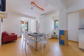 Un saló modern amb una taula de dinar, cadires blanques, un sofà vermell i una cuina amb nevera.