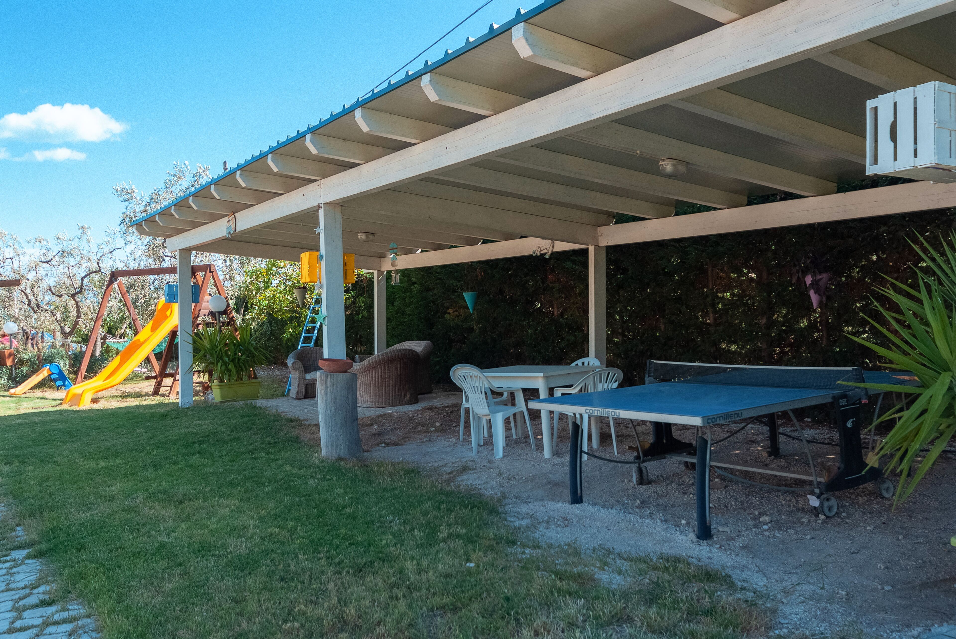 Un espace extérieur abrité comprenant une table de ping-pong, des chaises et un toboggan.