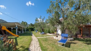 Un espace extérieur ensoleillé avec un chemin en pierre, un toboggan jaune et un fauteuil de jardin bleu.