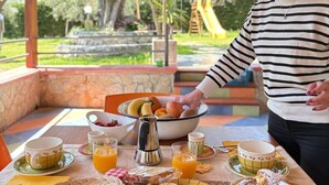 Un espace extérieur abrité, aménagé pour prendre les repas, avec une table dressée pour le petit-déjeuner, comprenant des fruits, des viennoiseries et des boissons.