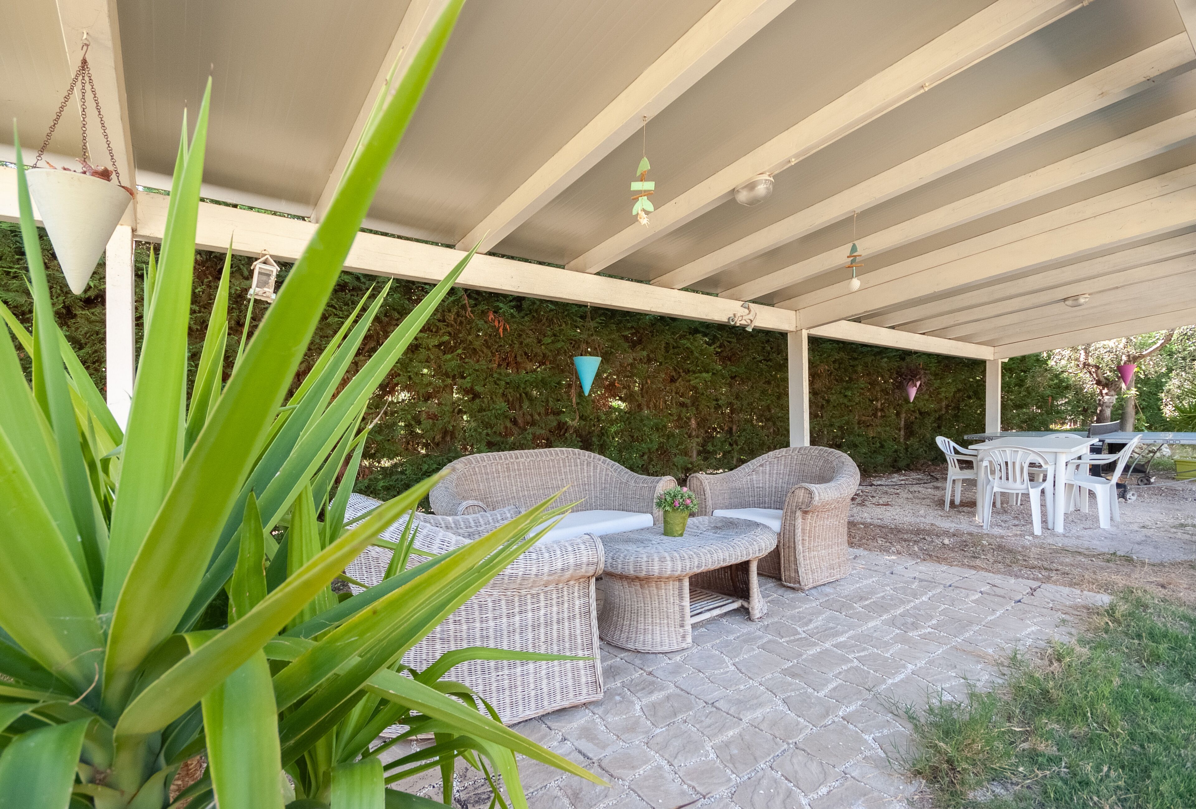Un patio couvert aménagé avec des meubles en osier, une table et des chaises.