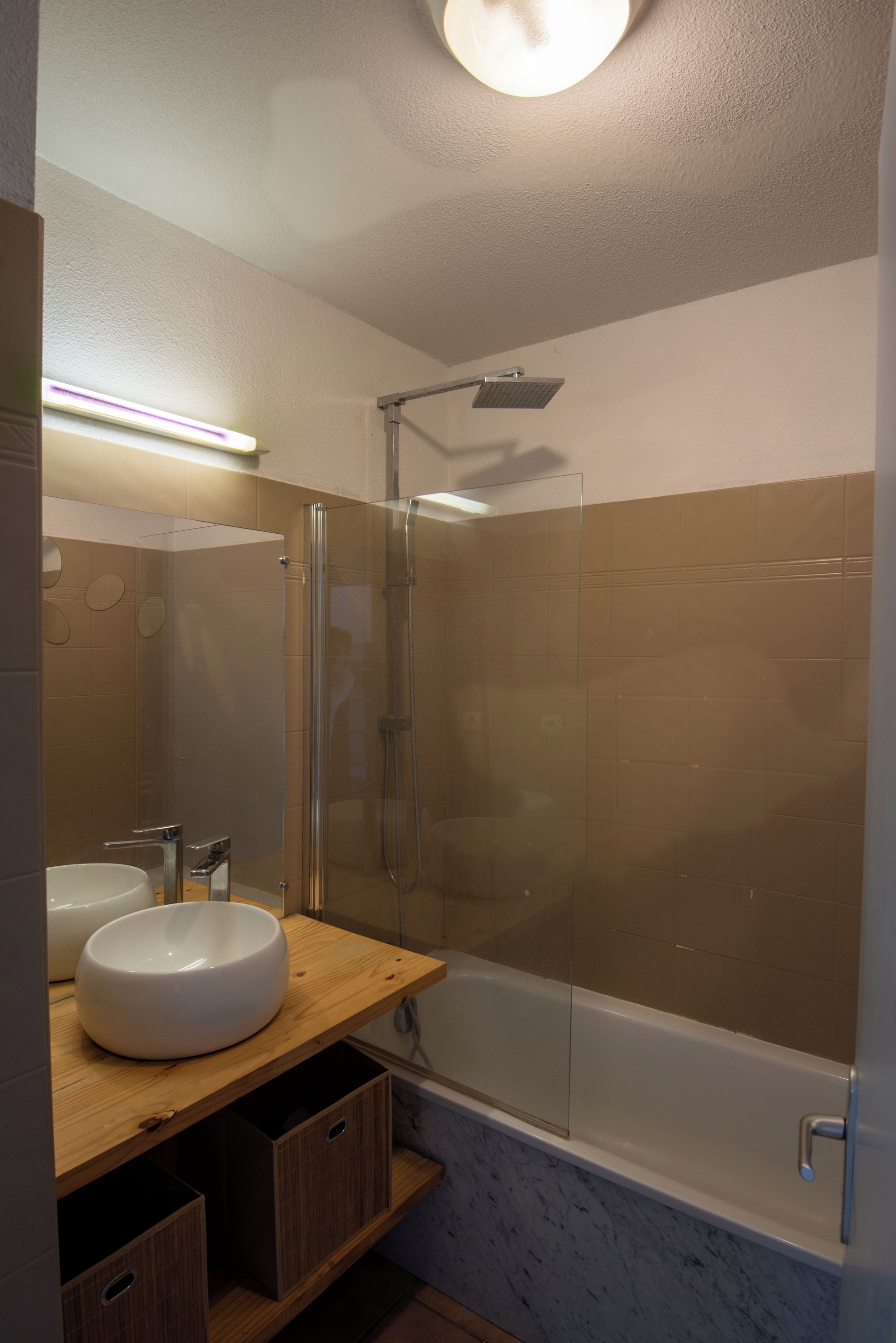 Ein modernes Badezimmer mit einer gläsernen Duschkabine, einer weißen Badewanne und einem Holzbadezimmermöbel mit großem Waschbecken.