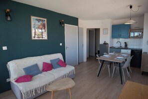 A modern living space with a white sofa, a dining table set for four, and a kitchen area with blue cabinets. - Superb T2 (sleeps 4-6) sea and Port Argeles in residence with pool (Argelès-Sur-Mer)