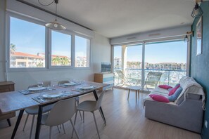 A modern living space with a dining area, a balcony with a view, and a sofa with cushions. - Superb T2 (sleeps 4-6) sea and Port Argeles in residence with pool (Argelès-Sur-Mer)