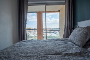 A hotel room with a large bed, a view of a marina, and a balcony with a cityscape. - Superb T2 (sleeps 4-6) sea and Port Argeles in residence with pool (Argelès-Sur-Mer)
