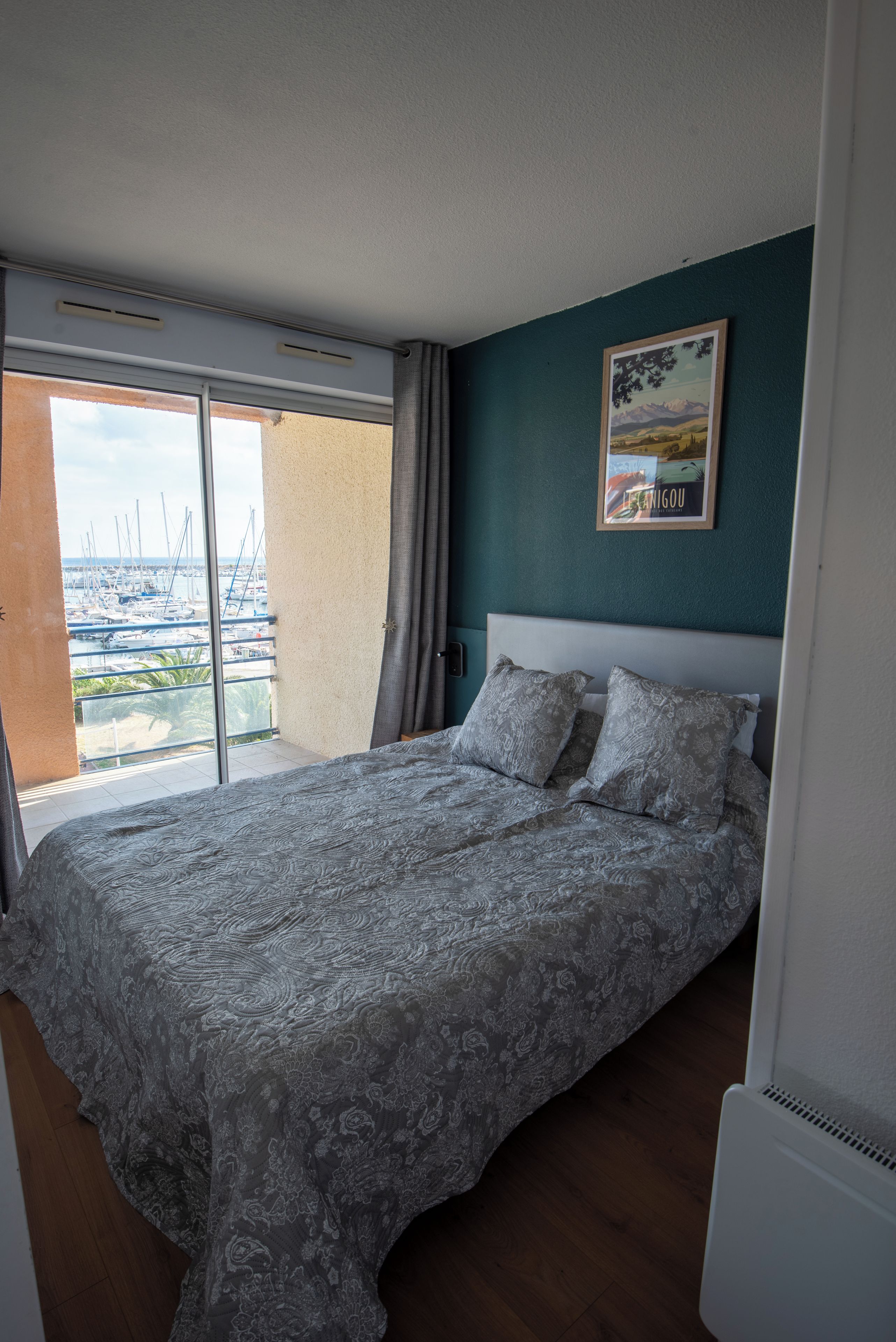 Une chambre avec un lit, une fenêtre donnant sur les bateaux et un tableau accroché au mur.