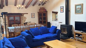Ein Wohnzimmer mit Holzbalkendecke, einer Sofagarnitur, einem Fernseher und einem Kamin.