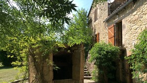 Un edificio de piedra con una entrada rústica, rodeado de vegetación y un sendero de grava.