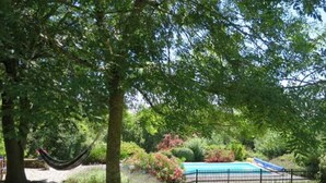 Un jardín con árboles, una hamaca y un área cercada con piscina.