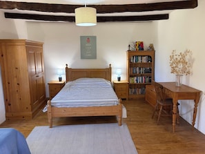 A bedroom with a wooden bed, bedside tables with lamps, a bookshelf, and a desk with a vase of dried flowers.