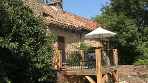 Un edificio rústico de piedra con una terraza de madera y una sombrilla.