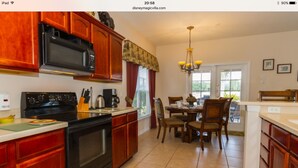 Una cocina con armarios de madera, microondas, estufa y comedor con sillas y mesa.