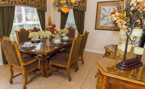 Uma sala de jantar com mesa de madeira posta para seis pessoas, rodeada por cadeiras estofadas.