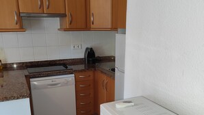 Een keuken met houten kastjes, een witte vaatwasser, een magnetron en een waterkoker.