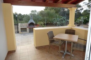 An outdoor patio with a table and chairs, a stone fireplace, and a view of the surrounding garden. - apartment/ flat - El Pilar de la Mola (El Pilar de la Mola)
