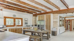A spacious kitchen with wooden beams, a dining area, and a view of the living room.