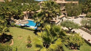 A resort with a swimming pool surrounded by palm trees and a mountainous backdrop.