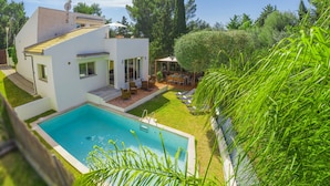 Una casa moderna con piscina, un patio con mobiliario exterior y un jardín.
