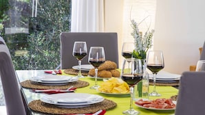 Una mesa de comedor dispuesta con platos, cubiertos, vasos y comida, con vistas a la vegetación exterior.