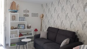 Un saló amb un sofà gris fosc, una estanteria blanca i un paper pintat amb motius.