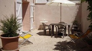 Un petit pati amb una taula i cadires, un parasol blanc i una planta en test.