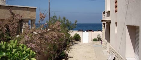 Um beco estreito com vista para o mar, ladeado por edifícios com paredes de pedra e fachada branca.