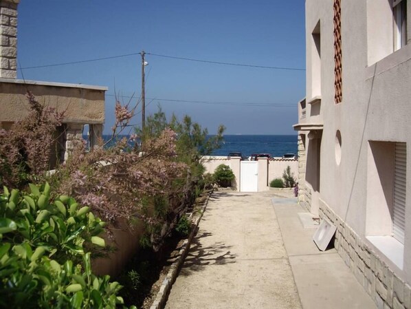 A narrow alleyway with a view of the sea, surrounded by buildings with stone walls and a white facade.