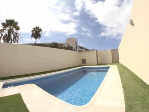A swimming pool with a clear blue water, surrounded by a white wall and a green lawn. - FABULOUS DUPLEX C6 WITH PRIVATE POOL (Adeje)