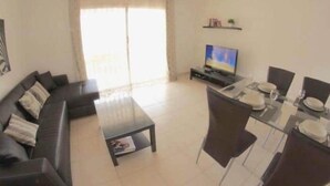 A living room with a sofa, TV, dining table, chairs, and a small coffee table. - FABULOUS DUPLEX C6 WITH PRIVATE POOL (Adeje)