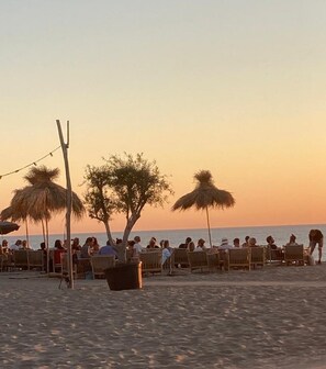 A beachside seating area with wooden chairs and thatched umbrellas, overlooking the ocean.