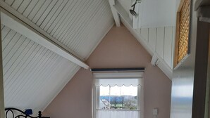 Un dormitorio con techo inclinado, una ventana con vistas, una cama con ropa de cama blanca y un cabecero de metal.