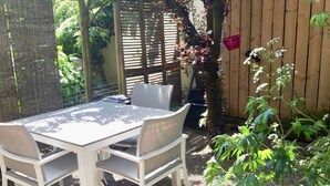 Un patio con una mesa y sillas blancas, rodeado por una cerca de madera y follaje.
